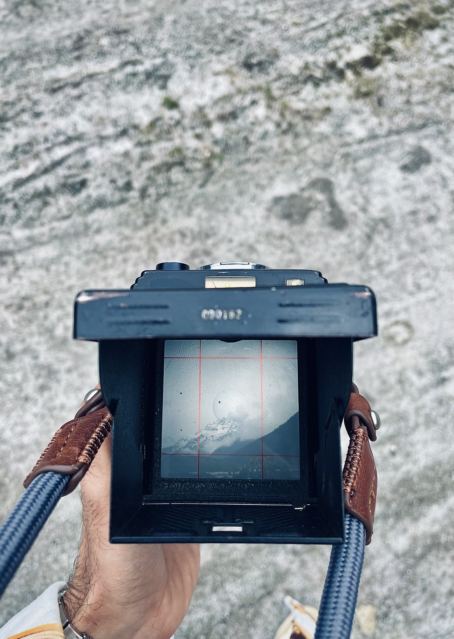 Looking down into the waist-level finder of a Yashica Mat 124G; a mountain sits on the ground glass above rocky ground.